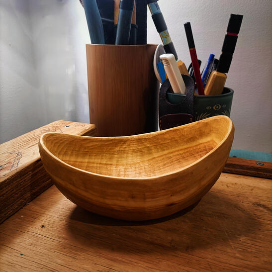 a bowl sits on a workspace alongside pots of various craft items