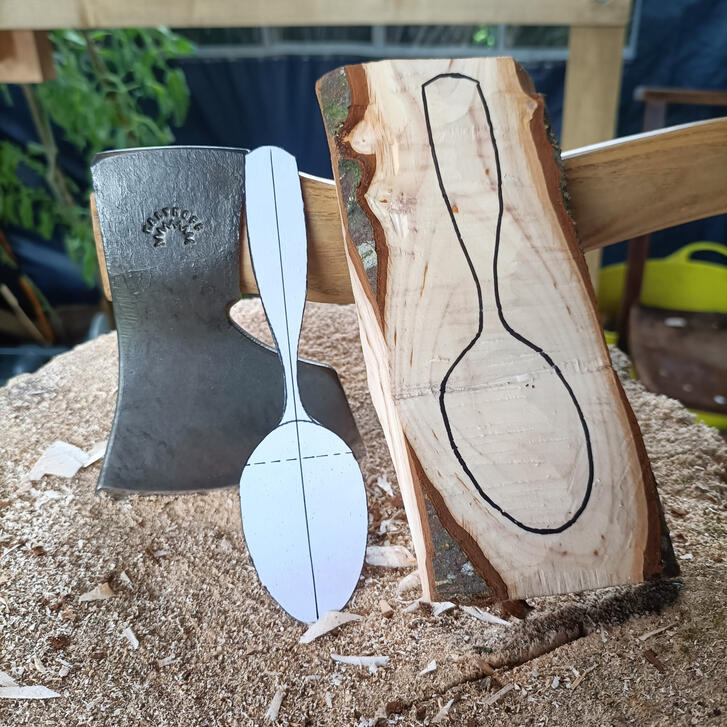 a spoon template and roughed blank rest atop a carving block and a kalthoff carving axe