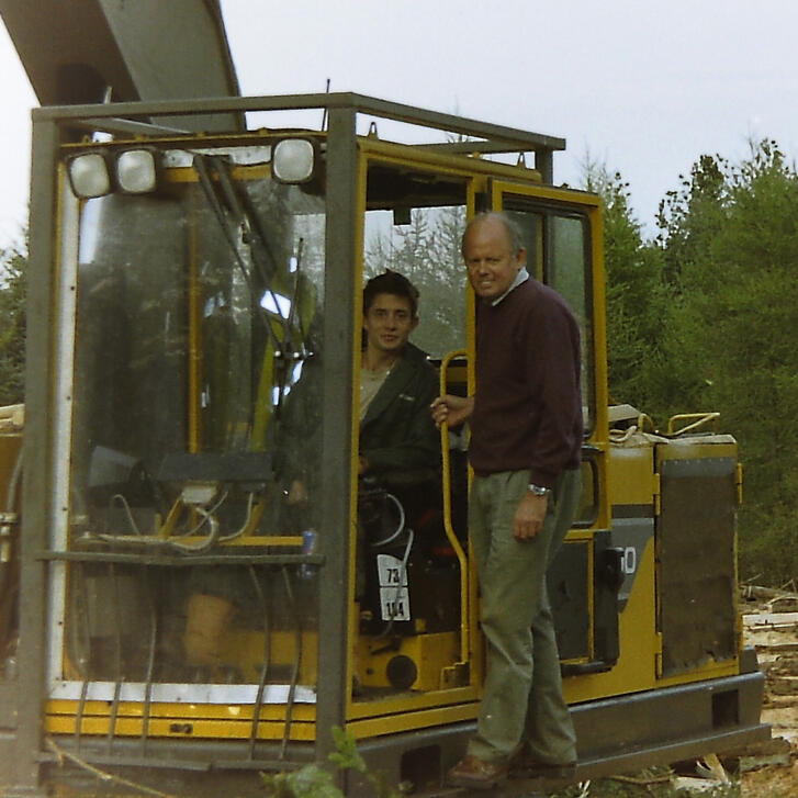 The maker Nick sits alongside his father on the side of his forest harvesting machine, the appearance is of an old style excavator