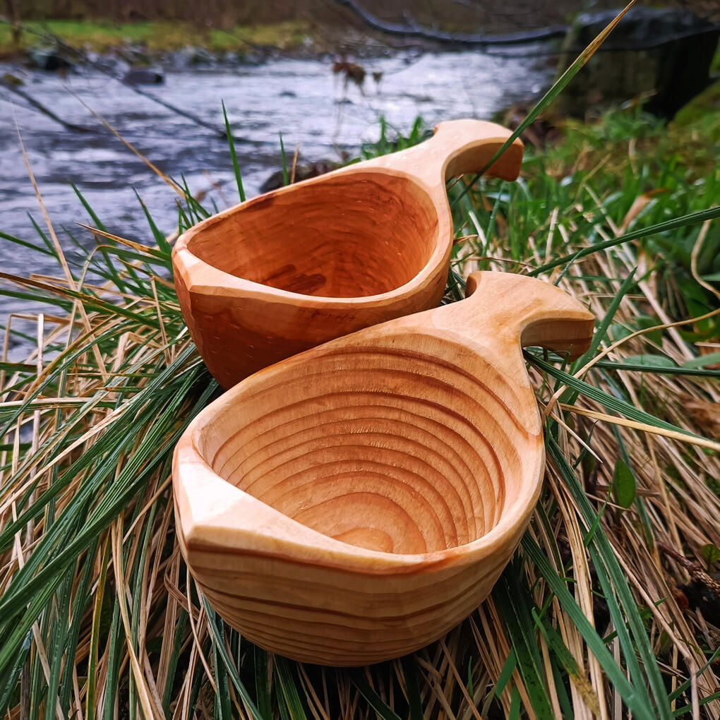 two sami kuksa cups sitting in a reed bed next to a fast flowing cheviot river